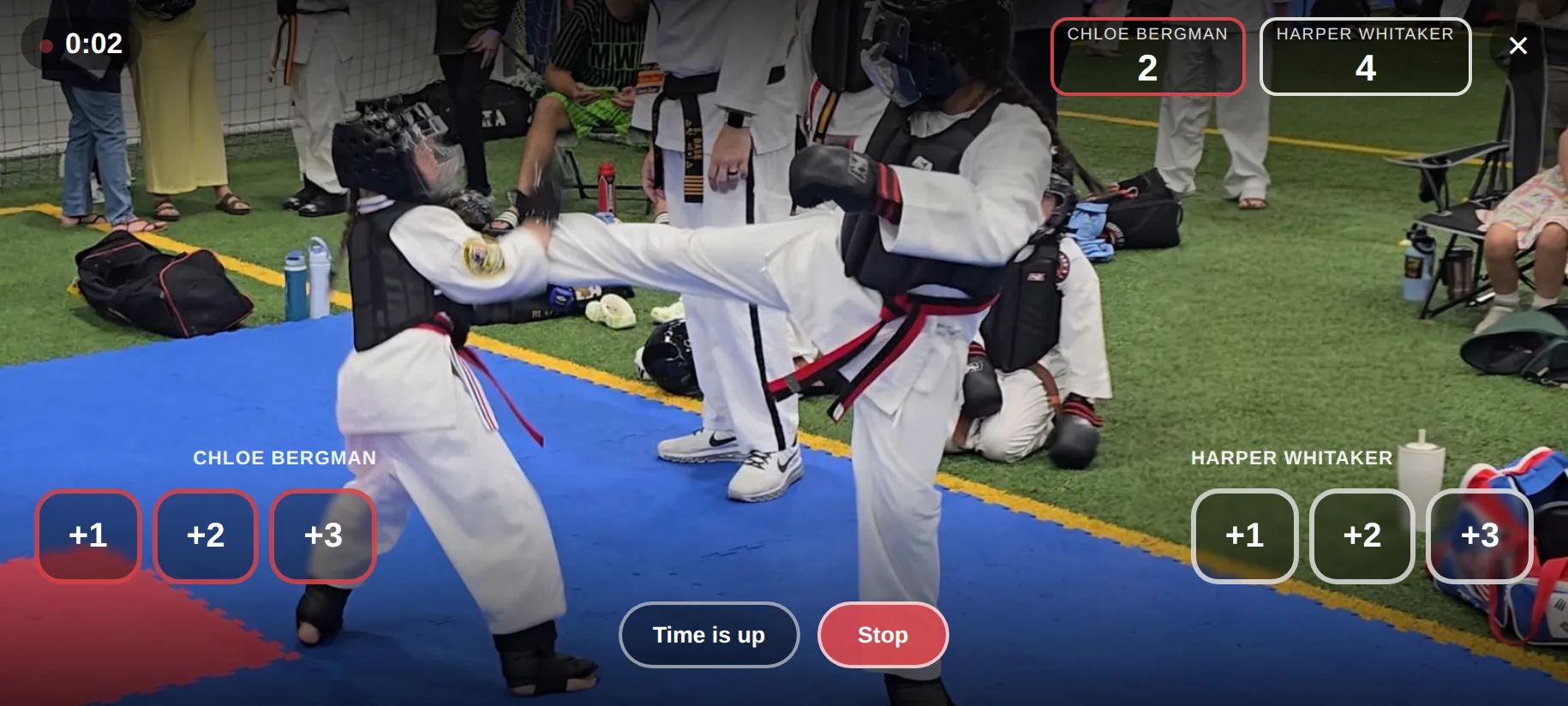 A sparring match being filmed and scored at the same time: the clock running, both competitors named with their running totals, and a bank of point buttons under each corner.